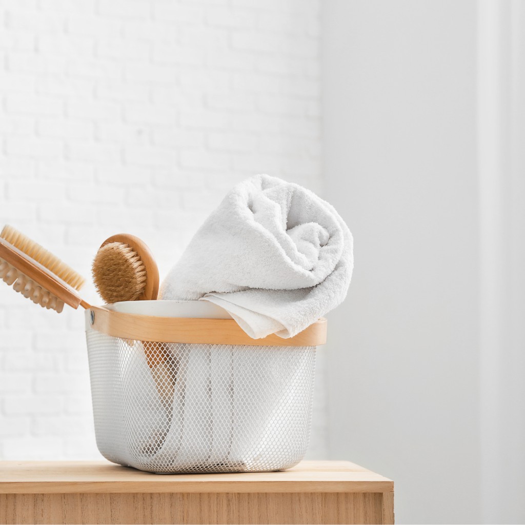 Wire basket with towel and body brushes on warm wood — Texture First ritual